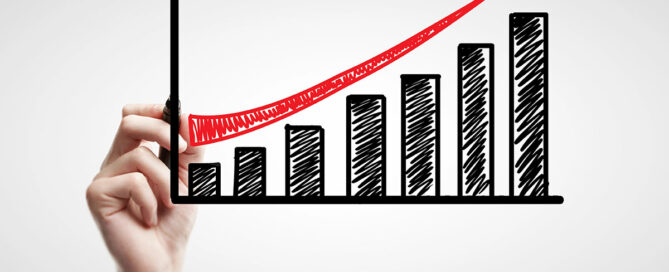 A hand is drawing a bar graph showing upwards growth on a dry erase board.