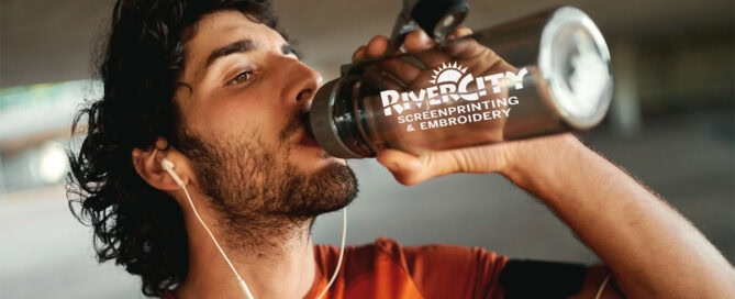 A man is drinking out of a reusable water bottle branded with a company logo.