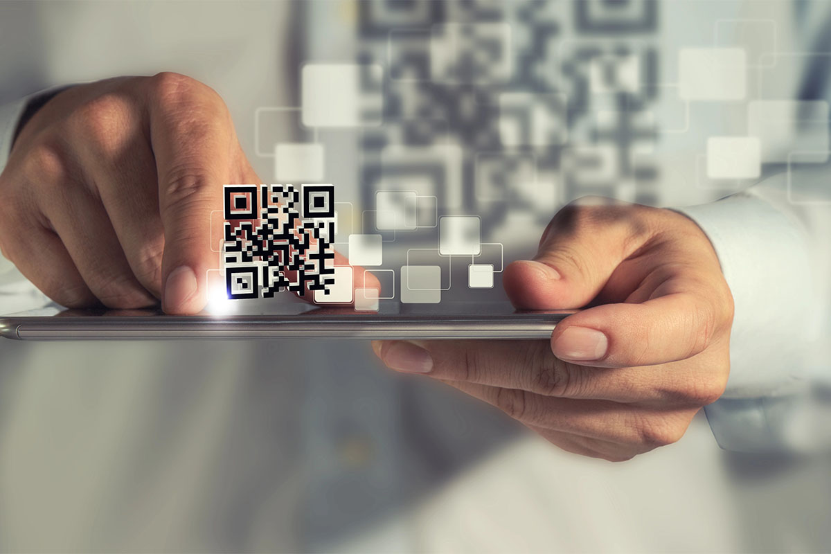 A close-up of a person's hand holding a smartphone, with a QR code displayed prominently on the screen and digital graphics of squares in the background.