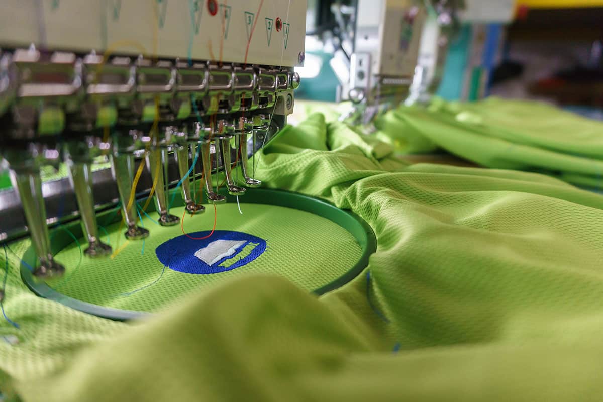 Embroidery machine creating Green Rivercity Screenprinting logo on lime green fabric.