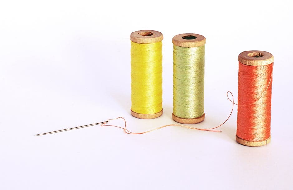 Spools of yellow, green, and orange thread with a sewing pin, representing custom embroidery and screen printing services.