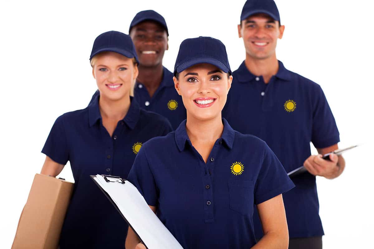 A group of four smiling individuals in navy blue polo shirts and caps, two holding clipboards and one carrying a box, standing together against a white background.