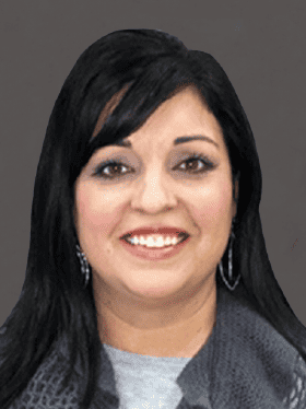 A smiling woman with long black hair and earrings, wearing a gray top and scarf, against a dark background.