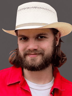 A young man with a beard and long hair smiles, wearing a white straw hat and a red shirt. The background is a solid dark color.