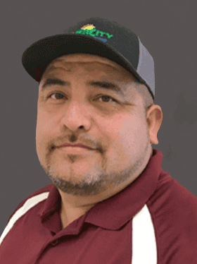 A man with a goatee wearing a dark maroon shirt and a black cap with a logo, posing against a gray background.