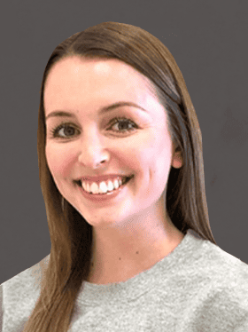 A smiling young woman with long brown hair wearing a gray sweatshirt, against a dark background.
