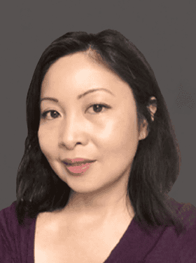 A woman with shoulder-length black hair, wearing a deep purple top, smiles softly against a neutral gray background.