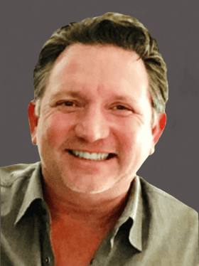 Smiling man with short dark hair, wearing a light gray shirt, against a dark background.
